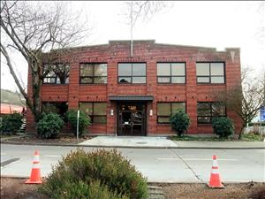 Two story brick building with large windows. Traffic cones in the foreground. 